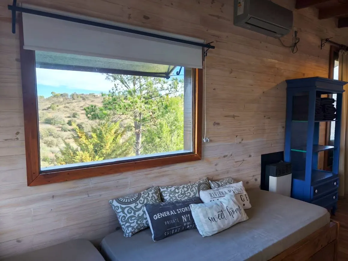Living de la Cabaña Chuña 2 con aire acondicionado y ventanal a las sierras
