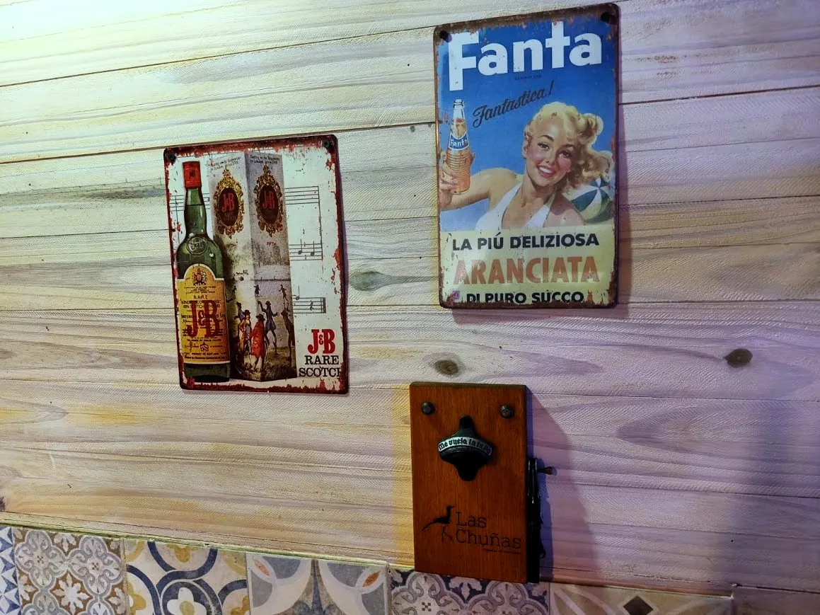Carteles vintage de chapa y destapador con el logo Las Chuñas en la pared de madera