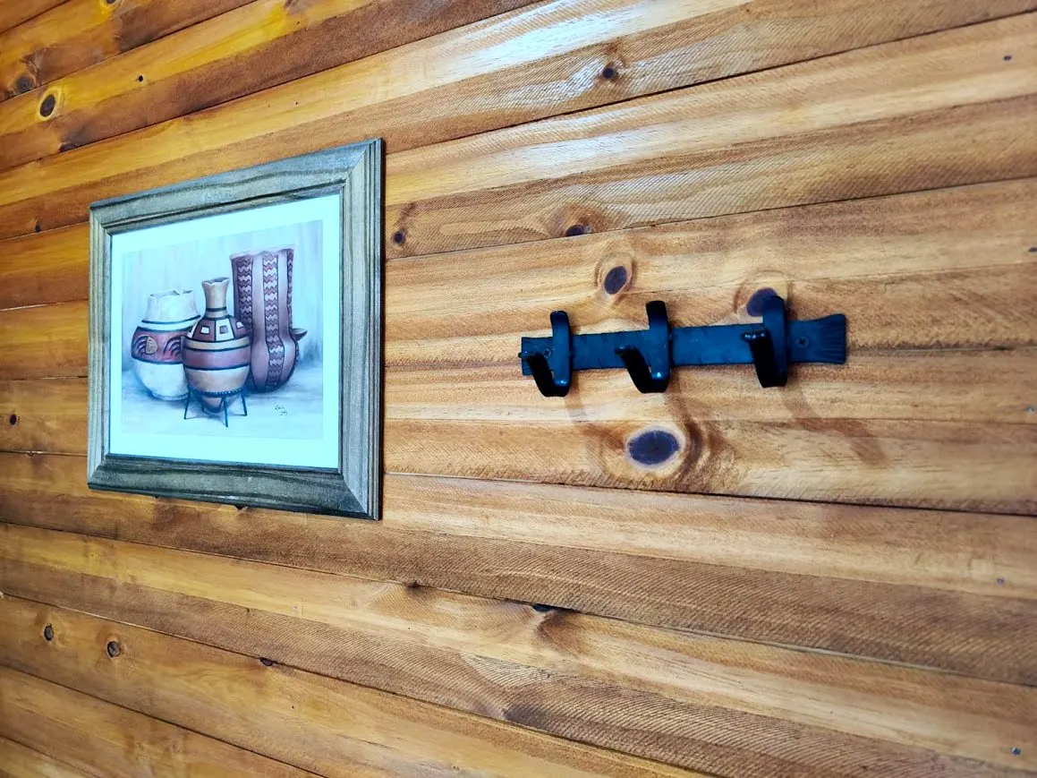 Cuadro de cerámica precolombina y percheros de hierro sobre pared de madera