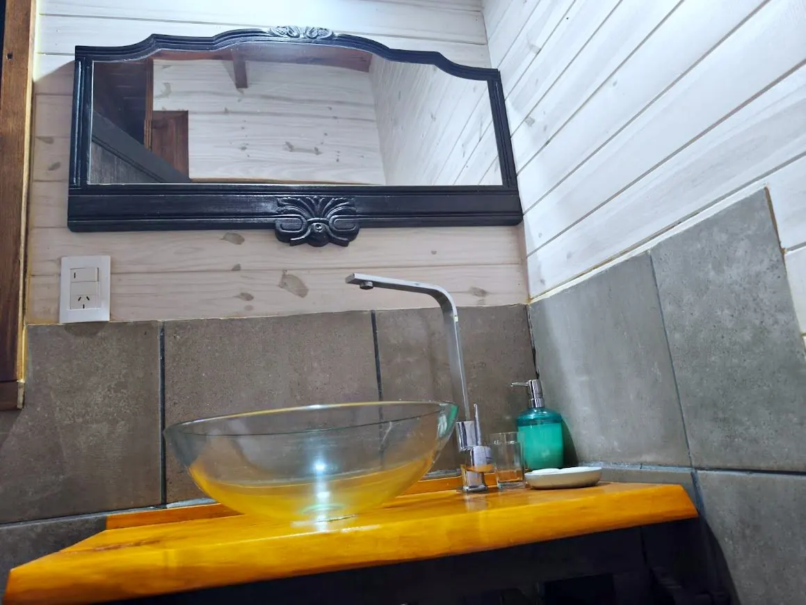 Baño con espejo antiguo, bacha de vidrio y revestimiento de madera